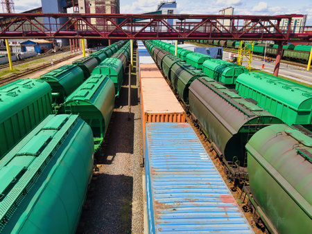 Colorful freight cars stretch across a bustling railroad yard, showing vibrant greens and blues. The sun casts sharp shadows, highlighting the busy industrial environment.の写真素材