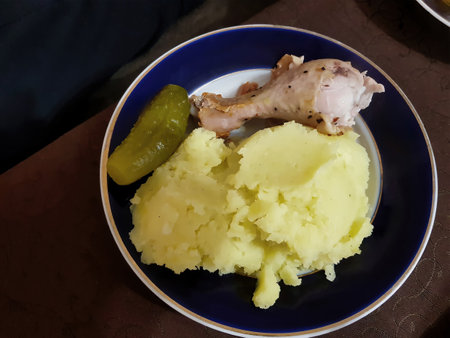 A comforting meal features fluffy mashed potatoes, a juicy chicken drumstick, and a tangy pickle, all presented on a vibrant plate during a friendly family dinner.の写真素材