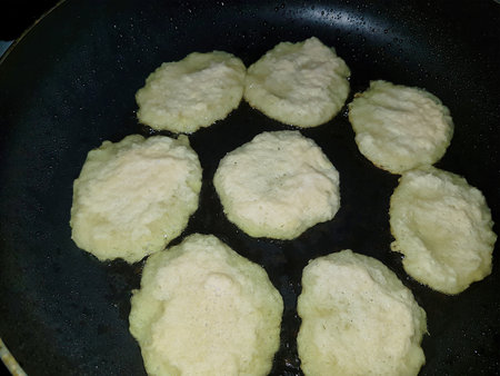 Fritters sizzle in a frying pan as they cook to a perfect golden color, creating a delightful aroma in the kitchen during a lively cooking session.の写真素材