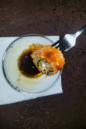 Delicate sushi roll, perfectly fried and crispy, is lifted by a fork, ready to be dipped in rich, flavorful sauce at an upscale dining location.の写真素材