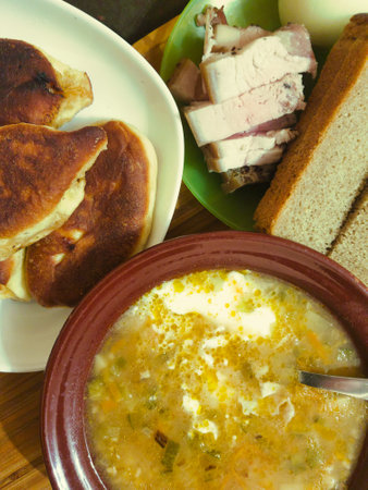 A hearty soup served in a brown bowl, accompanied by rustic bread, sliced meat, and golden pancakes, creating a comforting and inviting dining experience.の写真素材