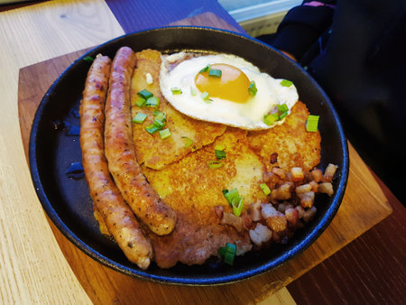 A delightful breakfast spread showcases crispy sausages, golden potatoes, and a perfectly cooked sunny-side-up egg, enjoyed in a warm, inviting cafe setting.の写真素材