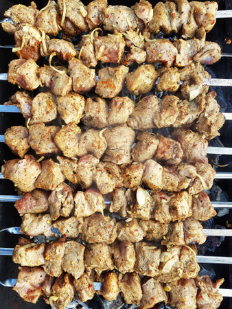 Mouthwatering pieces of marinated meat sizzle on skewers, infused with spices and herbs, creating a delicious aroma at a vibrant outdoor celebration.の写真素材