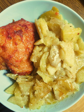 A delicious plate features a golden-brown piece of fried chicken and a warm mix of apples and potatoes drizzled in a creamy sauce, inviting a cozy meal.の写真素材