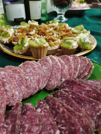 A delightful assortment of thinly sliced cured meats graces a green platter, accompanied by beautiful pastries topped with fruits at a lively celebration.の写真素材