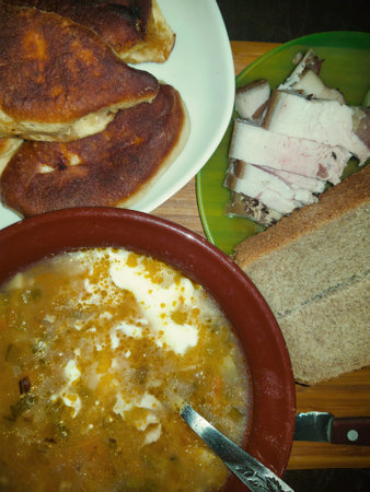 A hearty bowl of soup exudes warmth, paired with crusty bread, tender slices of meat, and golden pastries, creating an inviting meal perfect for sharing.の写真素材