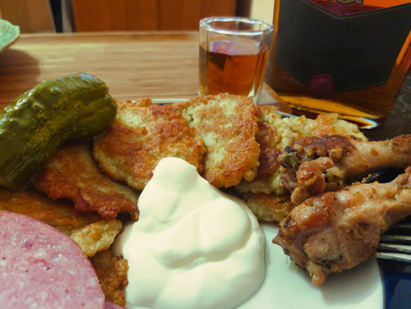 A delightful array of crispy potato pancakes, accompanied by succulent meat, tangy pickles, and a dollop of creamy sauce, enjoyed alongside a glass of spirit.の写真素材