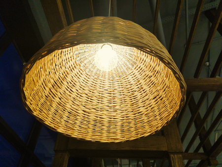 A beautifully crafted woven light fixture illuminates the space with a warm and inviting light, creating a cozy atmosphere in the cafe as night falls.の写真素材