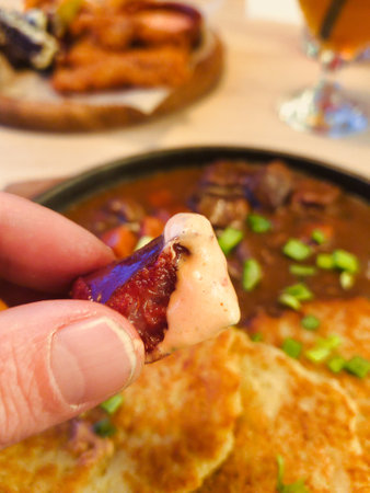 A hand holds a succulent piece of meat dipped in a rich sauce, capturing the essence of flavorful cuisines.の写真素材