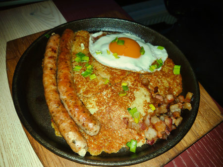 Brightly garnished breakfast spread includes crispy sausage links, a sunny-side-up egg, and a deliciously golden pancake with green onions sprinkled on top.の写真素材