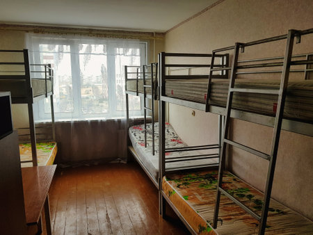 A bright dormitory room features metal bunk beds and colorful bedding, allowing ample space for students. Natural light floods in through large windows, enhancing comfort.の写真素材