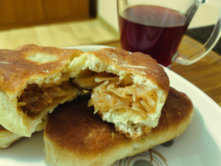 Soft, golden pastries are filled with flavorful cabbage, resting on a plate alongside a steaming cup of herbal tea. Perfect for an afternoon snack.の写真素材