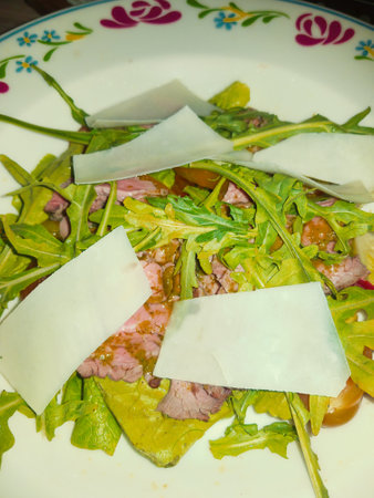 A delightful mix of greens topped with succulent slices of meat and creamy cheese, creating a harmonious blend of flavors and textures on a decorative plate.の写真素材