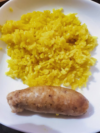 A hearty plate showcases vibrant yellow rice and a succulent sausage. This comforting meal invites enjoyment at any time of day, perfect for sharing.の写真素材