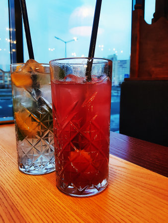 Two colorful cocktails with fresh fruit sit on a polished wooden table, creating a vibrant atmosphere as evening lights filters through the windows.の写真素材