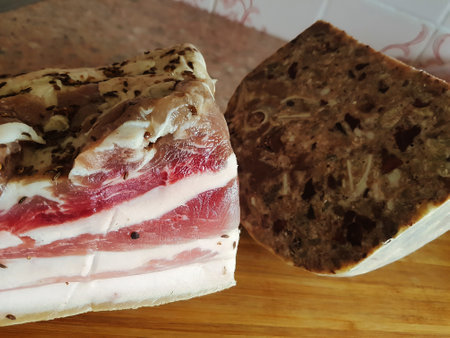 A close-up view reveals succulent marbled pork belly resting on a wooden board beside a rich, textured loaf of meat, symbolizing culinary craftsmanship.の写真素材