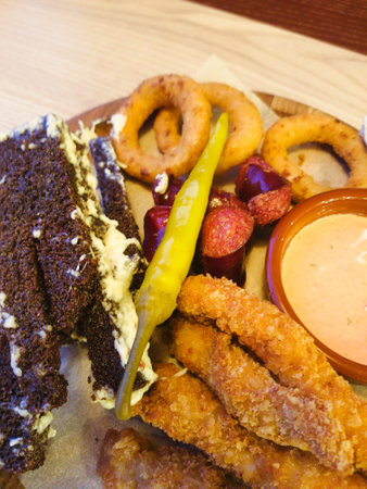 A vibrant platter showcases crispy fried chicken, onion rings, and tangy sauces besides a rich chocolate cake, perfect for sharing and indulging.の写真素材