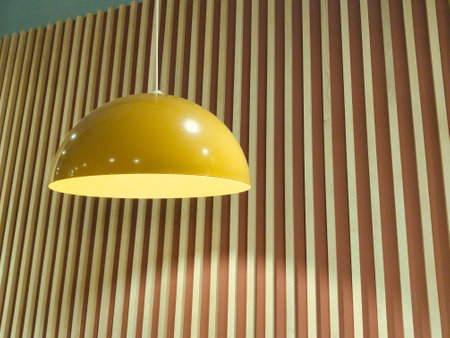 A vibrant yellow pendant light illuminates a stylish room, highlighting the textured striped wooden wall. The space exudes a contemporary charm and warmth.の写真素材