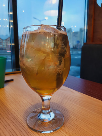 A glass filled with a chilled drink sits on a wooden table by the window, capturing the serene ambiance of a city evening as twilight sets in.の写真素材