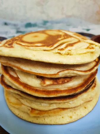 Fluffy, golden pancakes are stacked high on a blue plate, showcasing their perfectly cooked surfaces...