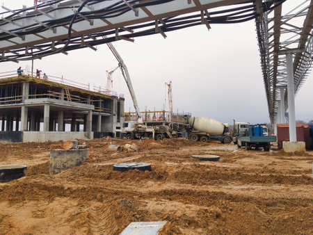 Workers are actively engaged in constructing a large building amidst a busy construction site, with machinery and equipment surrounding them during a cloudy day.の写真素材