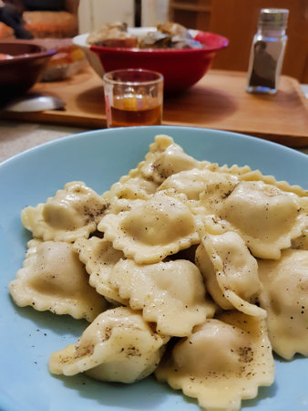 Steam rises from a plate filled with homemade ravioli, garnished with black pepper. In the background, a cozy meal setting awaits family bonding and shared stories.の写真素材