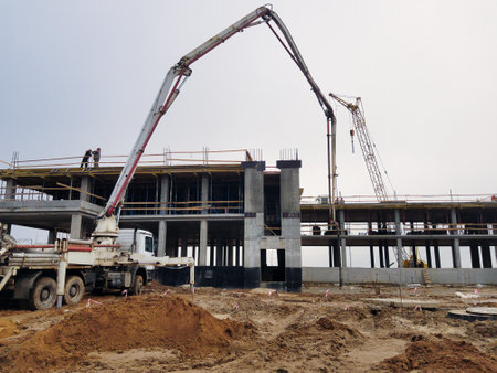 Workers are actively pouring concrete into molds at a construction site under cloudy skies, showing...