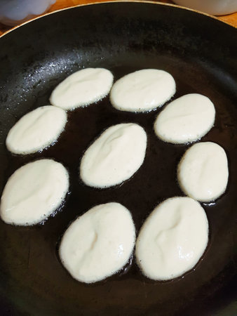 Round shapes of pancake batter sizzle in a hot skillet, bubbling gently as they cook. A cozy kitchen setting adds warmth to this breakfast moment.の写真素材