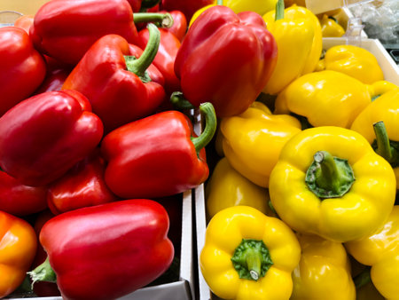 Bright red and yellow bell peppers fill boxes at a bustling market. Shoppers browse nearby, enjoying the vibrant colors and fresh produce available.の写真素材