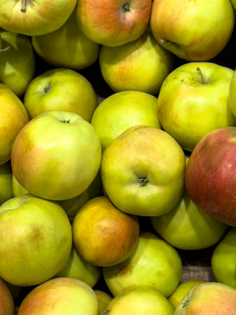 Bright green and yellow apples are stacked together in abundance at a local market, showing the...