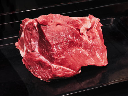 A large piece of fresh red meat sits on a sleek black surface, highlighting its quality and readiness for cooking or preparation in a kitchen environment.の写真素材