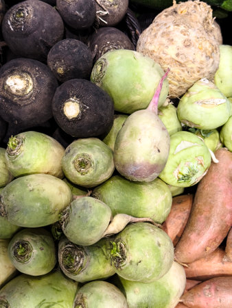 A vibrant array of root vegetables is on display, featuring turnips, sweet potatoes, and other varieties at a bustling market, perfect for autumn cooking.の写真素材