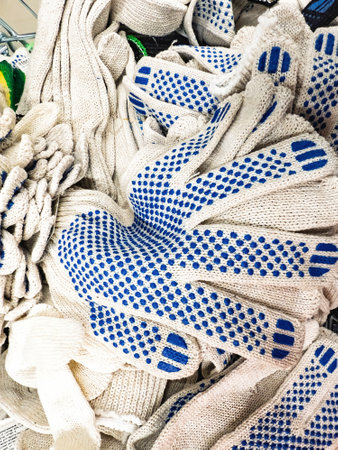 A collection of cotton gloves featuring blue gripping dots is seen piled together in a store. These gloves are intended for workers or DIY projects, providing safety.の写真素材