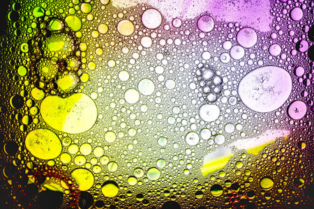 Intricate patterns emerge as droplets of liquid drift across a vivid background, revealing a fascinating interplay of color and light under a microscope.の写真素材
