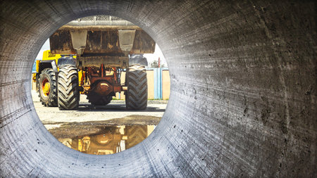 A large construction loader is passing through a concrete pipe. Mood and reflections are visible on the ground, illustrating the activity.の写真素材