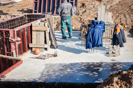A construction worker stands on a building site, surrounded by metal frames and tools, focusing on tasks in the bright daylight.の写真素材