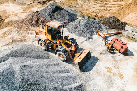 Heavy machinery works diligently to move and manage gravel piles at a construction site, showcasing industry activity and productivity under clear skies.の写真素材