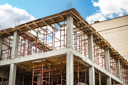 Workers are actively constructing a concrete structure, utilizing red scaffolding. The sky is clear...