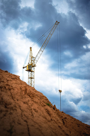 A large construction crane is positioned on a hillside, lifting materials while dark clouds gather overhead, indicating a change in weather.の写真素材