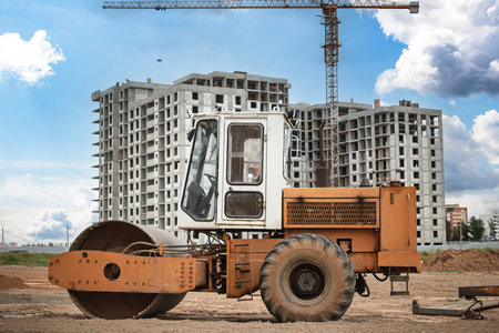 A heavy roller machine is positioned on a dust-covered construction site, working on ground...