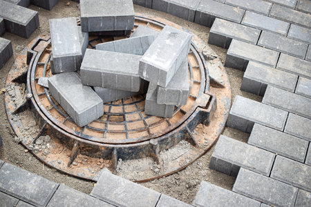 Gray bricks are stacked around a manhole cover in an urban construction zone, showing the process of creating a paved surface.の写真素材