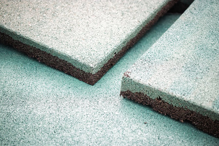 Close-up view of rubber flooring material showing its smooth texture and greenish tone. The flooring is being examined in a well-lit indoor setting.の写真素材