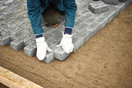A hard-working individual is carefully positioning concrete blocks on a prepared surface at a...