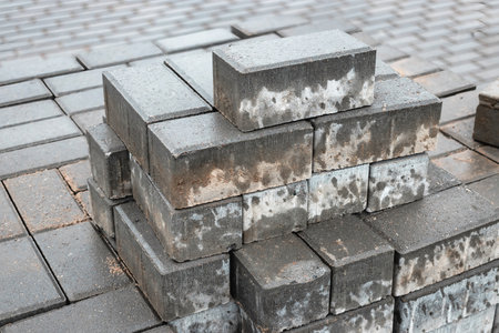 Workers arrange gray bricks in stacks at a construction site, showcasing an organized layout and...