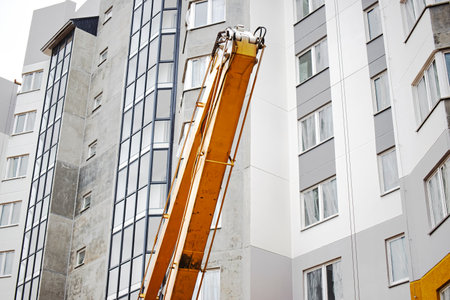 Workers utilize a crane to reach the upper floors of a high-rise apartment for maintenance and repair. Building has a sleek, contemporary design.の写真素材