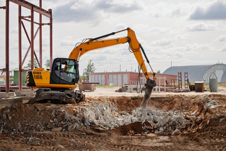 Heavy machinery is actively digging and moving stone and dirt at a construction site under a cloudy sky, indicating progress on the project.の写真素材