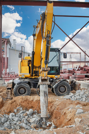 A heavy excavator operates at a construction site, drilling into rocky terrain. Bright blue skies and scattered clouds create a stark contrast with the ongoing work.の写真素材