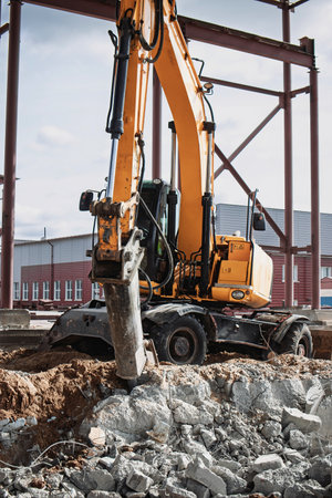 A construction worker operates an excavator, removing rubble from a site in a busy urban area. The...