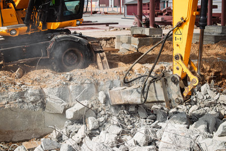 Heavy machinery breaks apart concrete as workers manage the construction site, showcasing progress...