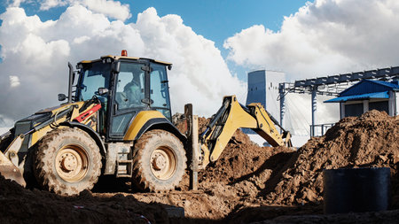 A backhoe loader is actively digging and moving earth at a construction site. The setting shows...